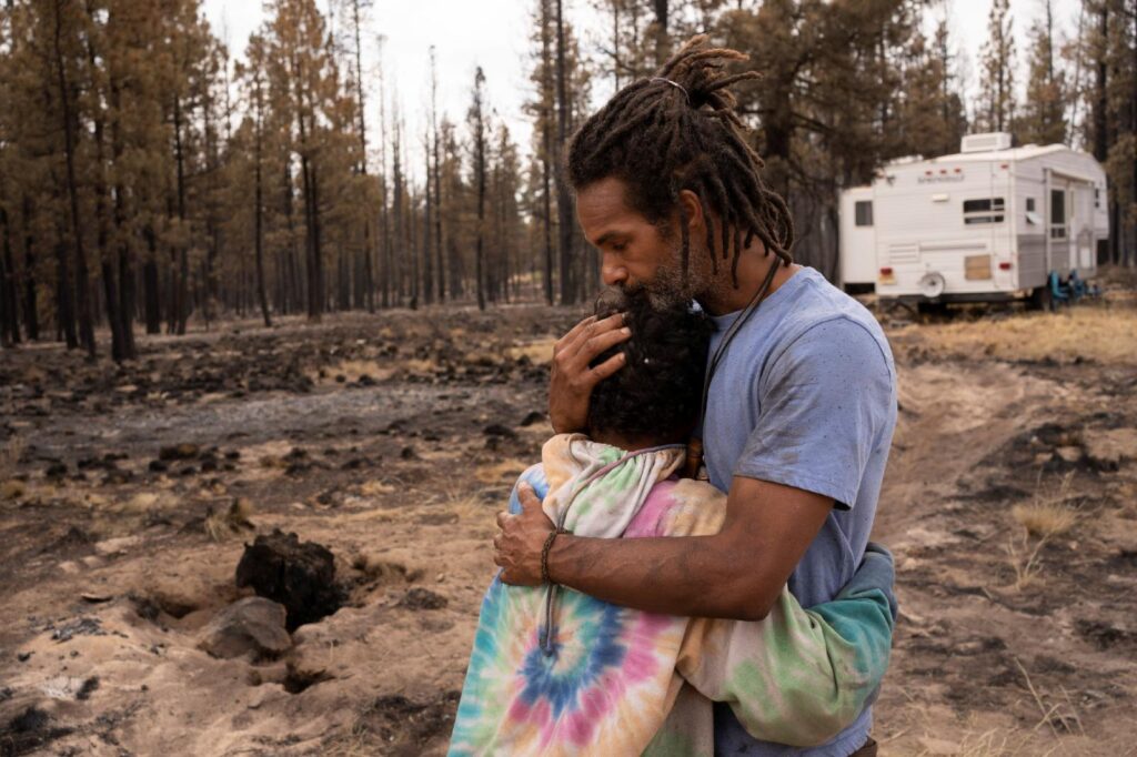 Nicolas Bey, 11, hugs his father, Sayyid Bey, within sight of a donated trailer they were using near Beatty, Ore., July 19, 2021, after their home was burned in the Bootleg Fire. (CNS photo/David Ryder, Reuters)