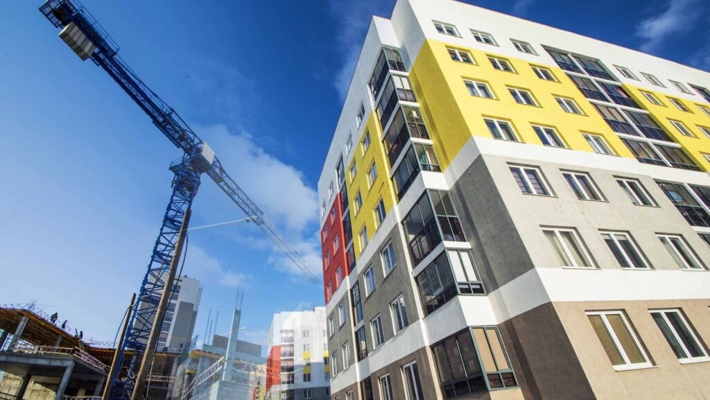 A photo of a Catholic Charities affordable housing project under construction. There's a large crane next to the building, which has modern color blocks in yellow, red and tan.