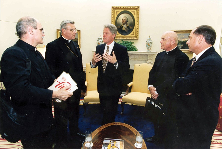 Then-President Bill Clinton meets in the Oval Office with a staff person and three priests, including Fr. Fred Kammer, then-president of Catholic Charities USA.