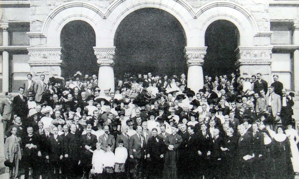 A black and white group shot of the founding of the National Conference of Catholic Charities. There are at least 100 people posed in front of a building on Catholic University's campus. 