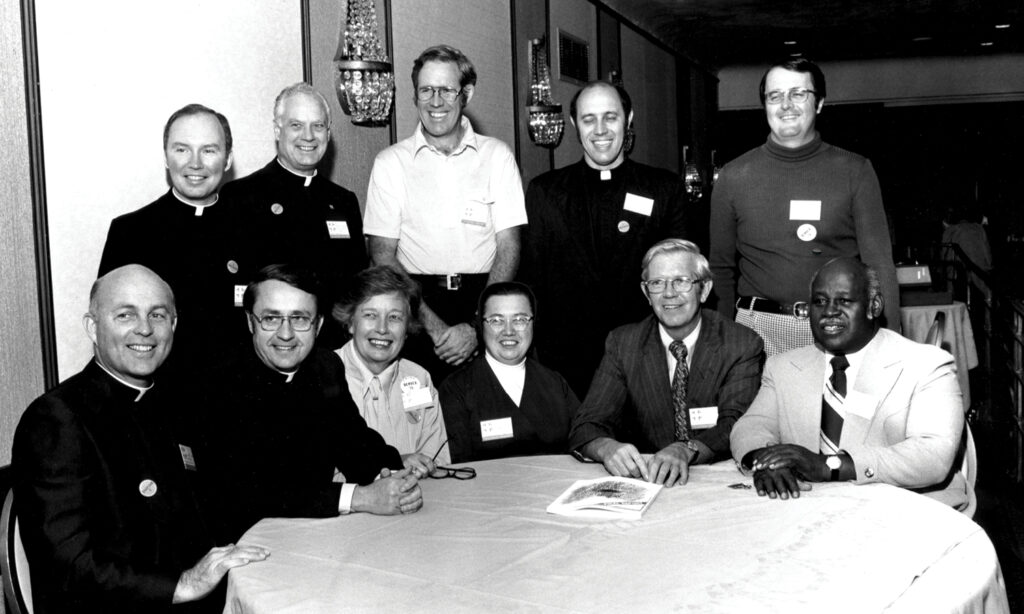 The authors of the Cadre Study gather around a table in this black and white photo. There are 11 people in the photo, half of them priests or nuns. 