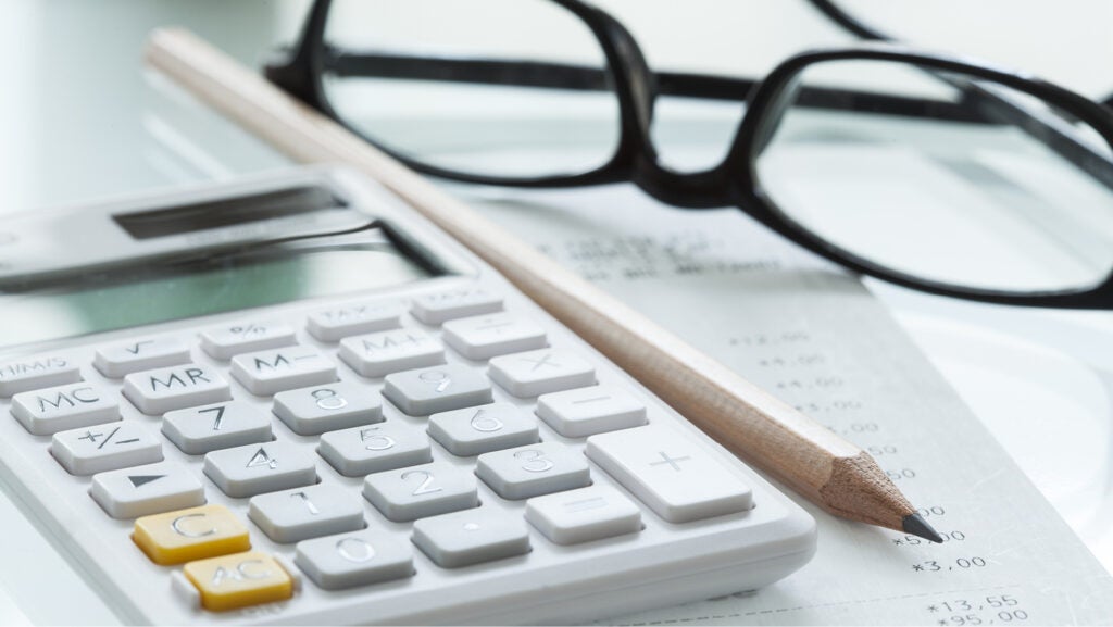 A closeup of a small calculator, a pen and a pair of folded black glasses.