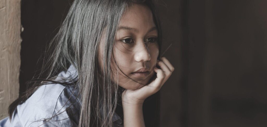 A girl with long dark hair rests her chin on her hand. She looks pensive.