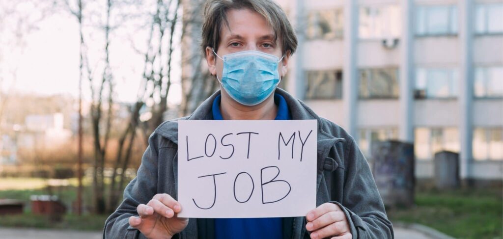A man with a covid mask stands outside holding a sign reading "Lost my job."