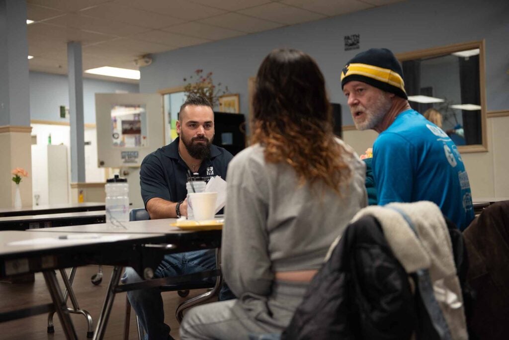 A Catholic Charities staff person meets at a long table with two clients to assess them for services.