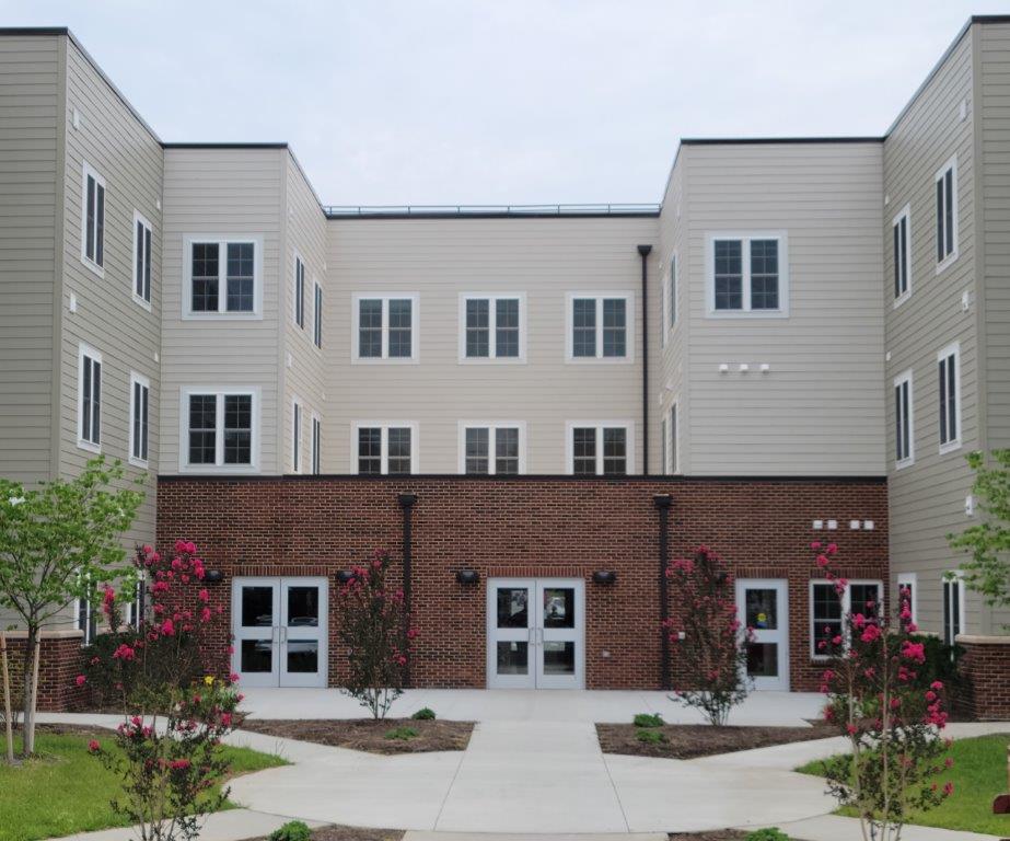 A new Catholic Charities affordable housing development. It's nicely landscaped, with hot pink crepe myrtle trees. The first floor is red brick and the three stories behind it are covered in tan siding. It has many windows, giving the appearance of light-filled apartment units.