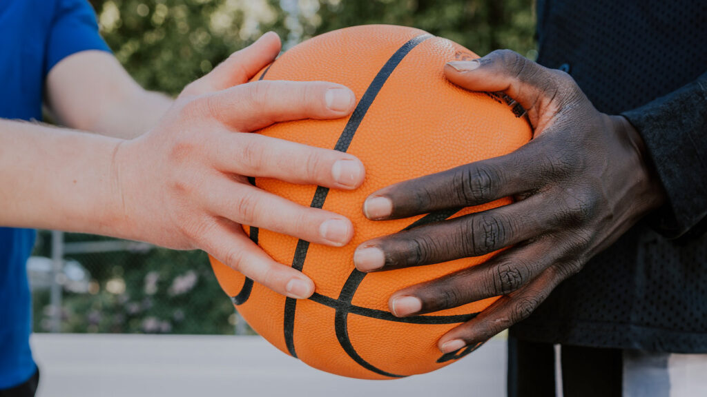 Two sets of hands -- one white, one black -- hold a basketball between them.