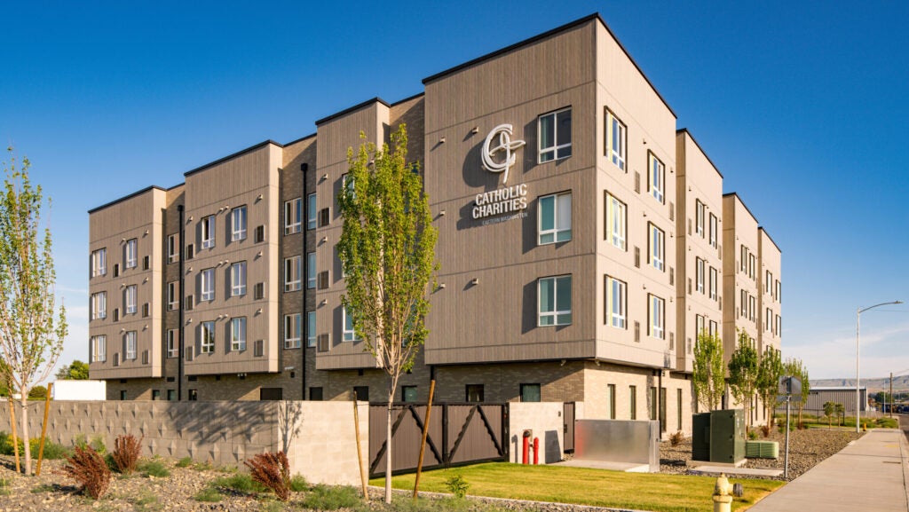 A large, modern sandstone apartment building that says Catholic Charities on the side. The grounds are neatly landscaped.