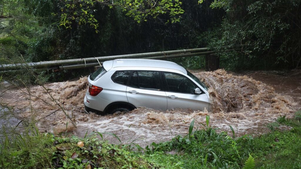 A silver crossover SUV is submerged in muddy floodwaters