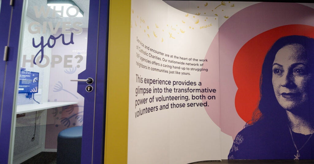 A photograph of the interior of the People of Hope Museum, showing a wall with an image of one of the museum's storytellers and facts about the Catholic Charities network's nationwide services to those in need.