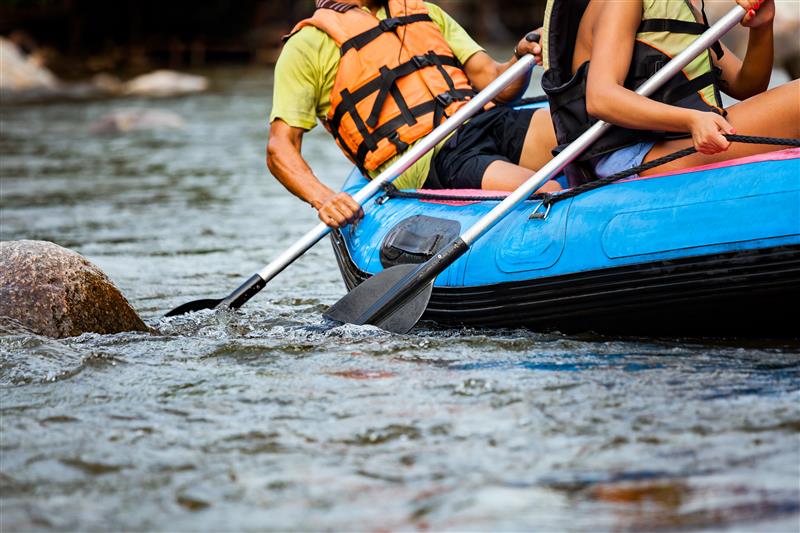 Wearing life vests and holding oars, a group sits on a blue raft in a river
