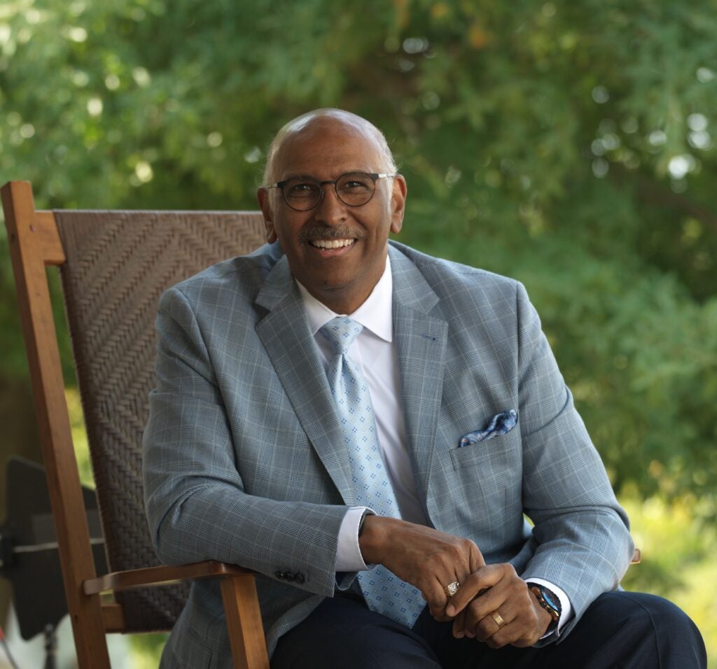 Michael Steele sits outside in a chair wearing a gray suit jacket and white shirt with a tie.